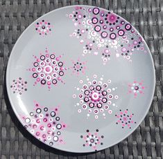 a white plate with pink and black designs on it sitting on a woven table cloth