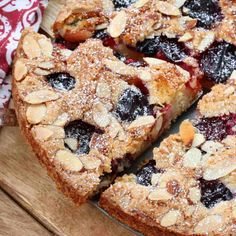 a pie with blueberries and almonds cut into slices on a cutting board next to a napkin