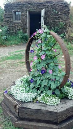 a wooden wheel with flowers growing out of it in the middle of a garden area