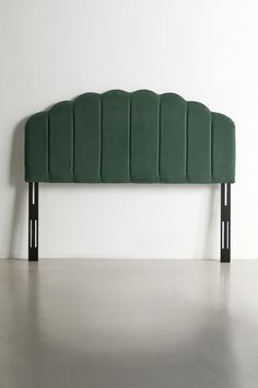 an upholstered headboard with black legs and green velvet fabric, against a white wall