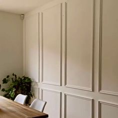 a dining room table with white chairs and a potted plant on the wall behind it