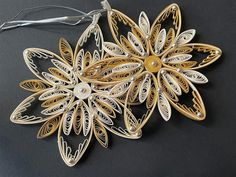 an ornament made out of gold and white paper with flowers on the side