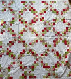 a quilted blanket with red and green squares on it, laying on the ground