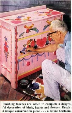 an old man painting a pink chest with hearts and flowers on the top, in front of a fireplace