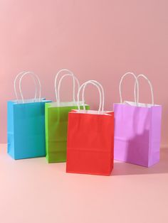 four colorful shopping bags are lined up against a pink background