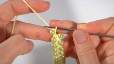 someone is knitting something with yarn on the end of a piece of yellow string and two hands are holding scissors