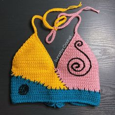 two crocheted swimsuits are sitting on a wooden surface, one is pink and the other is blue