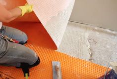 a woman in yellow gloves is working on an orange flooring mat with a hammer