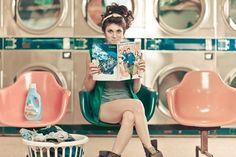 a woman sitting on a chair reading a magazine in front of a washer machine