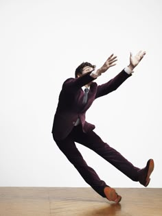 a man in a suit and tie is jumping on a wooden floor with his arms outstretched