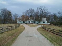 a large white house sitting on top of a lush green field next to a dirt road