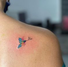 the back of a woman's shoulder with a small tattoo on it that says live