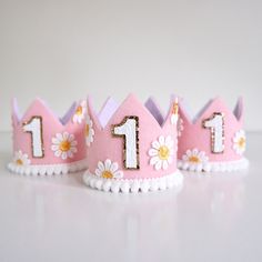 three pink crowns with white flowers and numbers one on each side, sitting on a table