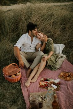 a man and woman sitting on top of a blanket next to each other in the grass