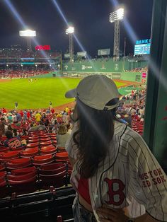 a woman standing in front of a baseball stadium filled with people watching the game at night