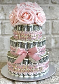 a three tiered cake with money and pink roses on top, sitting on a silver platter