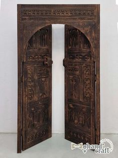 an open wooden door with intricate carvings on the doors and side panels, in front of a white wall