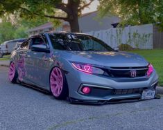 a gray car with pink wheels parked on the side of a road next to trees