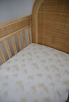 a bamboo crib with a white and tan palm print on the bed sheet, next to a wicker headboard