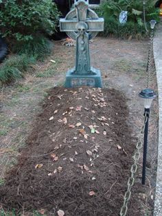 a grave in the middle of a garden filled with dirt and mulch next to a lamp post