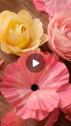 pink and yellow flowers are on a wooden table with one being held up by someone's hand