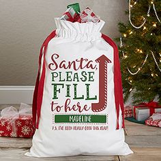 a white bag with santa's please fill to there on it sitting in front of a christmas tree