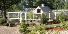 a white fenced in area with trees and bushes surrounding it, along with a house