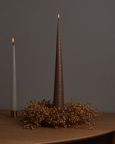 two tall candles sitting on top of a table next to some dry grass and flowers