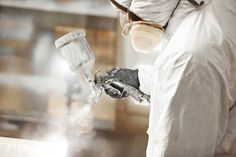 a man in white protective suit spraying water onto a piece of metal with a sprayer