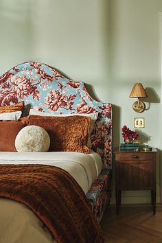 a bed with a floral headboard and pillows on it's sides, next to a night stand