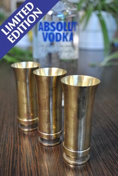 three brass shot glasses sitting on top of a wooden table next to a bottle of vodka