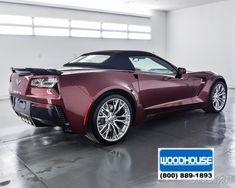 a maroon sports car is parked in a large room with white walls and flooring