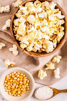 a wooden bowl filled with popcorn next to two white bowls full of corn kernels