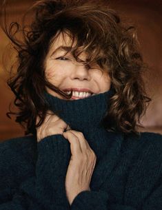 a woman with curly hair wearing a black turtle neck sweater and smiling at the camera