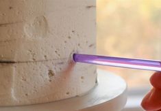 a person holding a purple object in front of a white cake