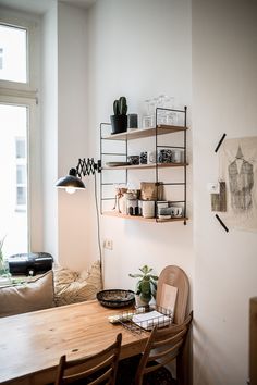 a wooden table sitting in front of a window next to a shelf filled with potted plants