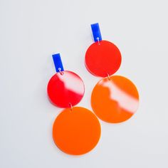 two red and one orange disc shaped earrings on a white surface with blue tags attached to them