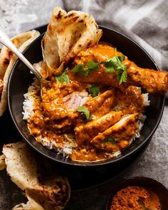 a bowl filled with chicken curry and rice next to pita bread on a table