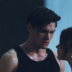 a man standing next to a woman in a black tank top and silver necklaces