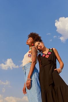 two women standing next to each other in front of a blue sky and white clouds