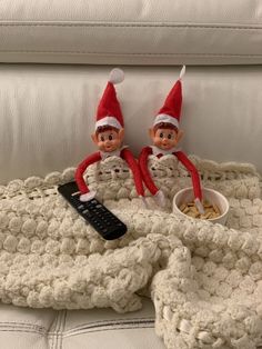 two elfs sitting on top of a couch next to a bowl of cereal and a remote control