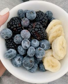 a person holding a white bowl filled with blueberries and banana slices on top of it