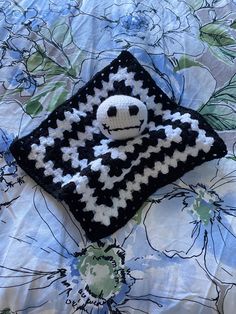 a black and white crocheted square with a smiley face on it sitting on a bed