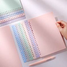 a hand holding a pen over a pink notebook with four different colored sheets on it