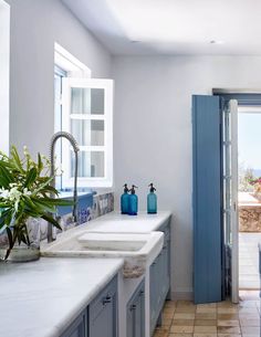 a kitchen with blue cabinets and white counter tops next to an open door leading to a patio