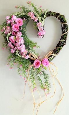 a heart shaped wreath with pink flowers and greenery hanging on the wall next to it