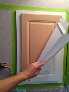 a person holding some white paper in front of a cabinet door that is being painted green