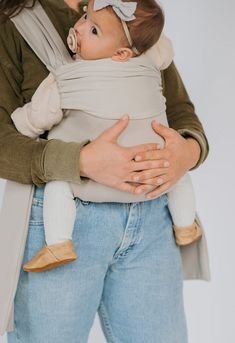 a woman holding a baby in her arms and wearing a wrap around it's neck