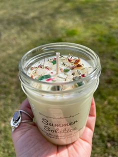 a hand holding a small glass jar filled with white liquid and sprinkles