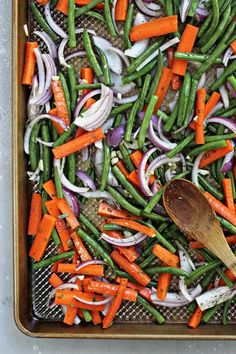 carrots, onions and green beans on a baking sheet with a wooden spoon in it